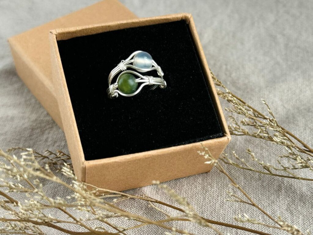 A picture of the product "Gemstone Adjustable Ring" Two rings are collected in a box with some dry flowers outside as decorations.